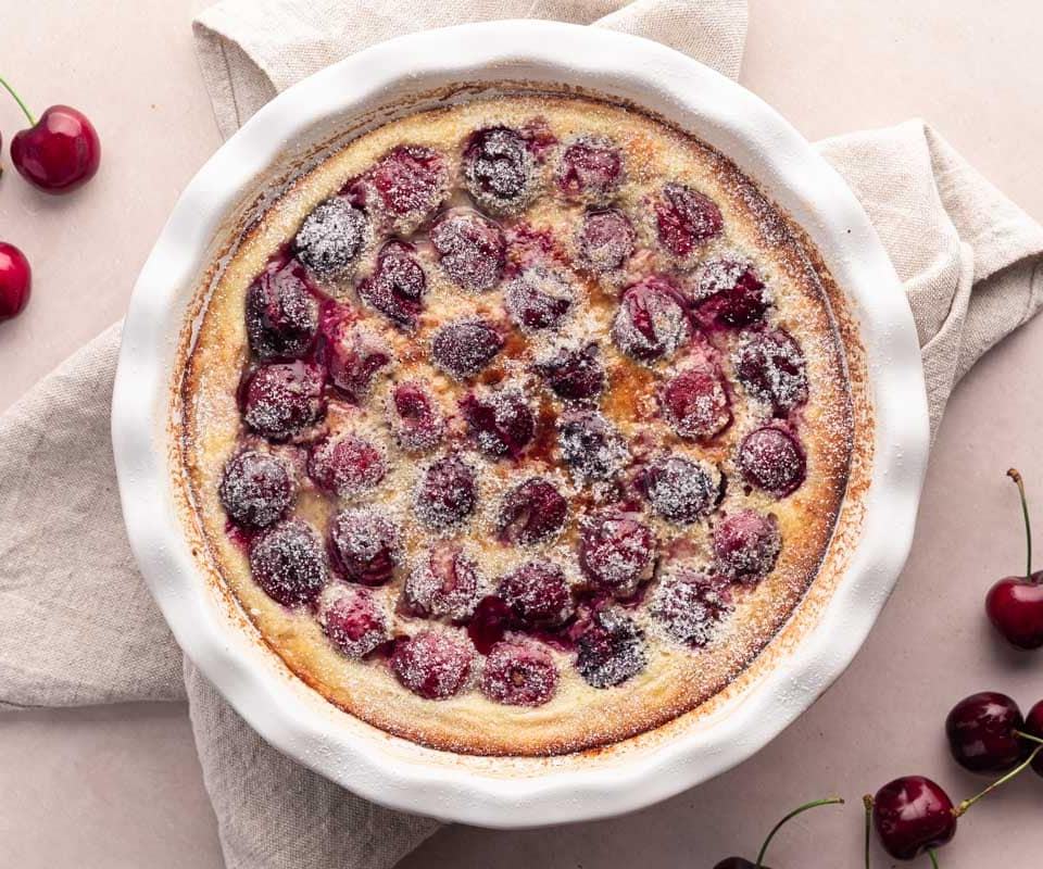 Baked clafoutis with dark sweet cherries and powdered sugar on top. Served to enjoy its delicate texture.