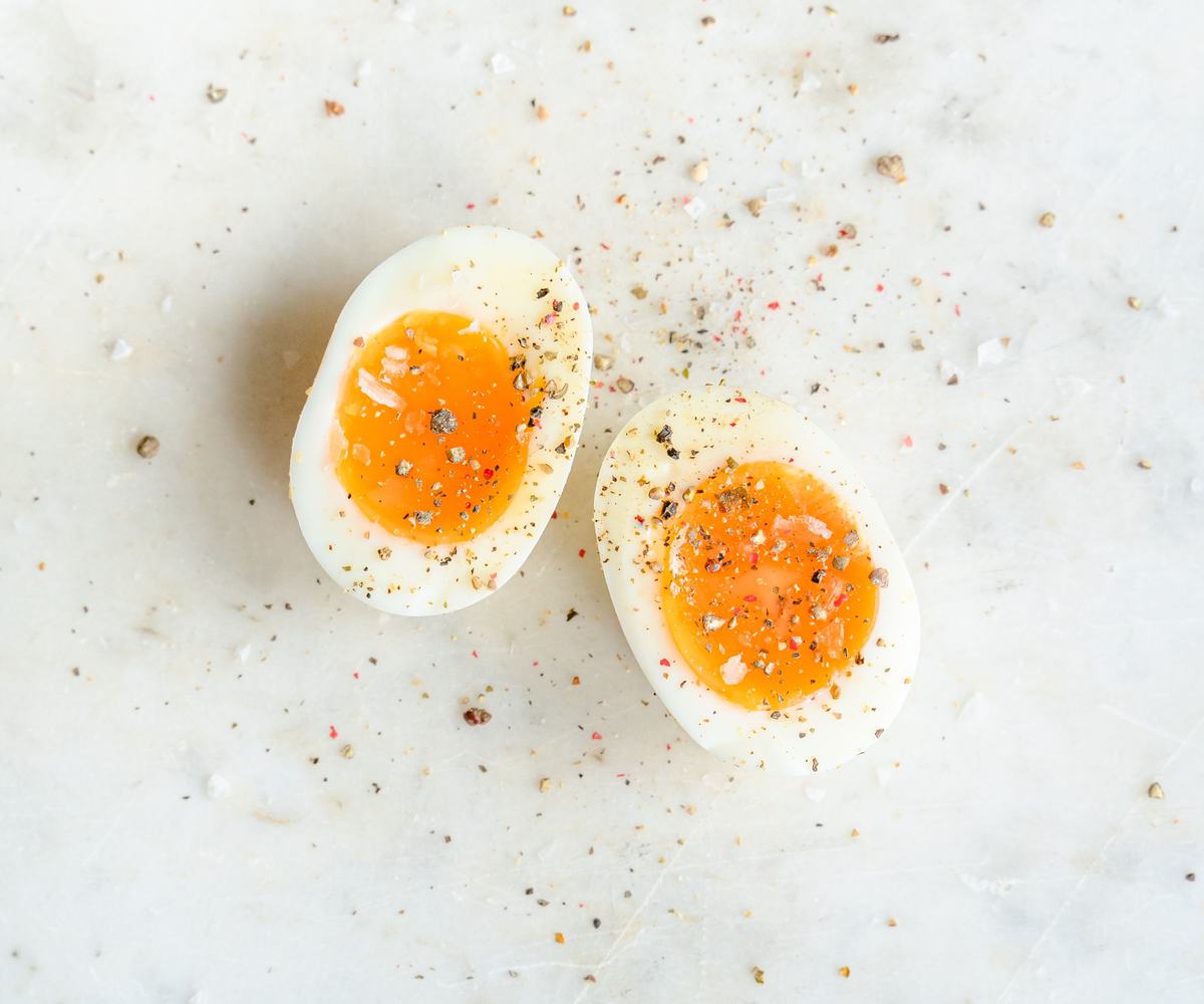 A halves of freshly soft-boiled egg with jammy yolk, sprinkled with salt and pepper on a light  surface.